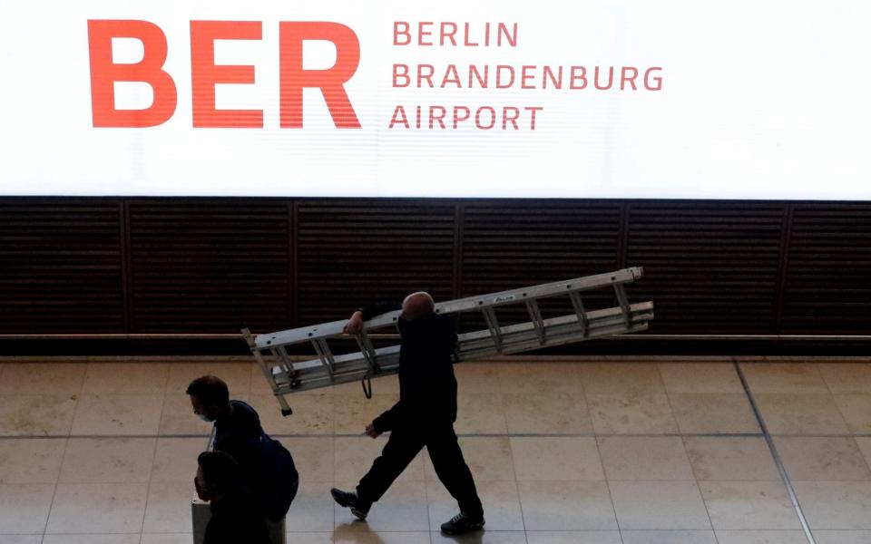 People walk past a display board before the official opening of the new Berlin-Brandenburg Airport - HANNIBAL HANSCHKE /REUTERS