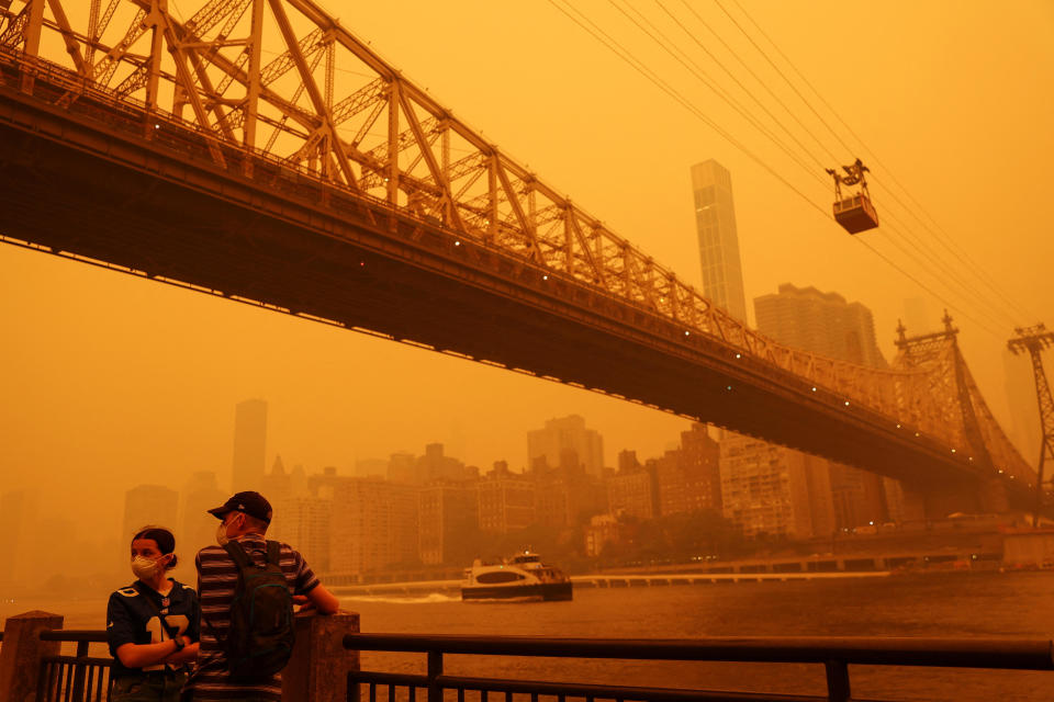 People wear protective masks as the Roosevelt Island Tram crosses the East River while haze and smoke from the Canadian wildfires shroud the Manhattan skyline in New York City, June 7, 2023. / Credit: SHANNON STAPLETON / REUTERS