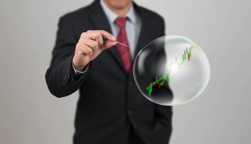 A man in a suit popping a bubble with a stock market chart in it.