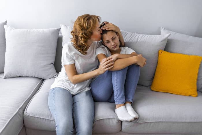 A mom kisses her daughter on the head as they sit on the couch