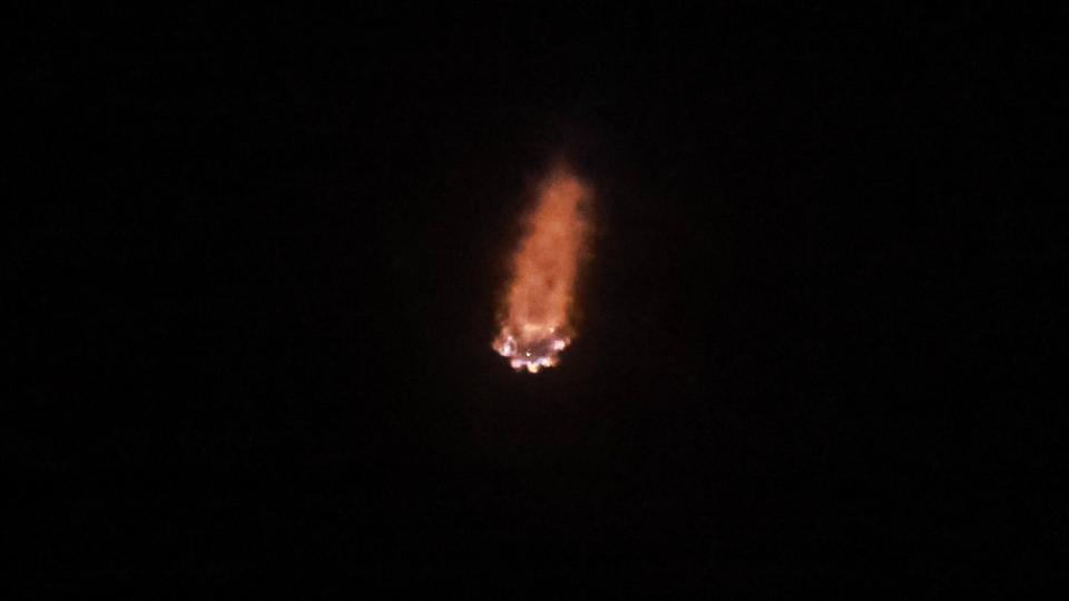 a white rocket lifts off at night above a plume of fire and smoke