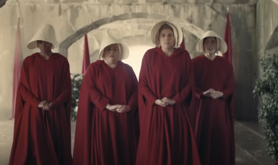 Kim Kardashian, another notable name, and two unidentified women wear red cloaks and white bonnets, reminiscent of outfits from "The Handmaid's Tale," standing solemnly