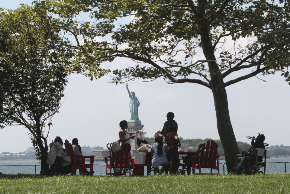 FILE - In this Aug. 4, 2012 file photo, the Statue of Liberty is shown in the background as visitors to Governors Island picnic in the shade in New York. The Statue of Liberty, which has been closed to visitors since Superstorm Sandy, is scheduled to reopen for tours on July Fourth, when Statue Cruises resumes departures for Liberty Island from Lower Manhattan. For tourists who want a photo of the famous statue without visiting the island, there are many options and vantage points, including from Governors Island. (AP Photo/Mary Altaffer, file)