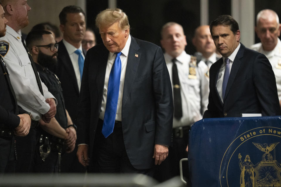 Donald Trump, in a suit and tie, stands surrounded by security personnel and police officers at a public event