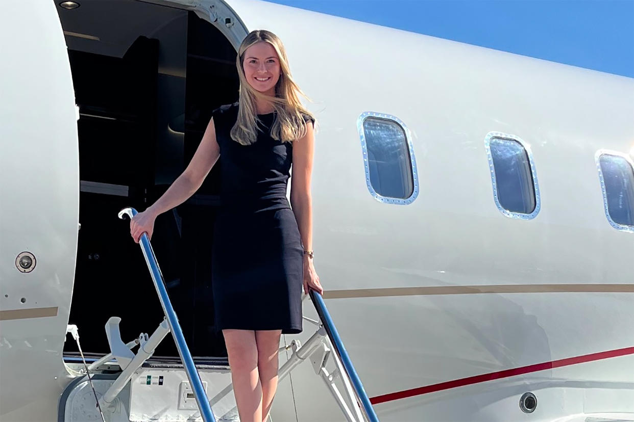 A blonde flight attendant in a black dress stands on the steps to a plane