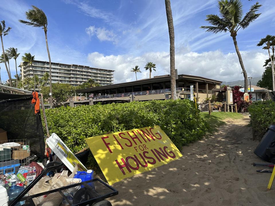 A sign rests at a protest camp in front of resort hotels and restaurants along Kaanapali Beach in Lahaina, Hawaii on Wednesday, Nov.14, 2023. A group of Lahaina wildfire survivors is vowing to camp on a popular resort beach until the mayor uses his emergency powers to shut down unpermitted vacation rentals and make the properties available for residents in desperate need of housing. (AP Photo/Audrey McAvoy)