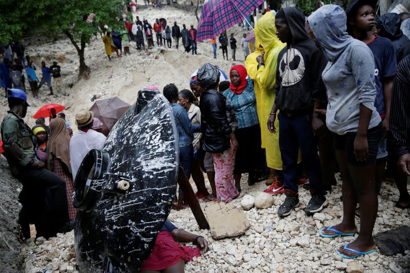 Residents look at the body of a woman who died during the passage of Tropical Storm Laura, in Port-au-Prince