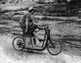 <p>A woman with her foot kicked over the handlebars sits atop a stationary scooter.</p>