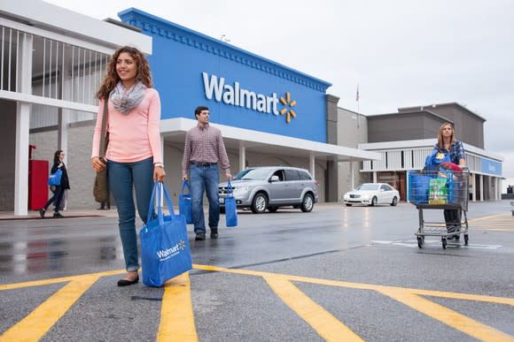 Several shoppers with bags and carts walking in front of a Walmart store.