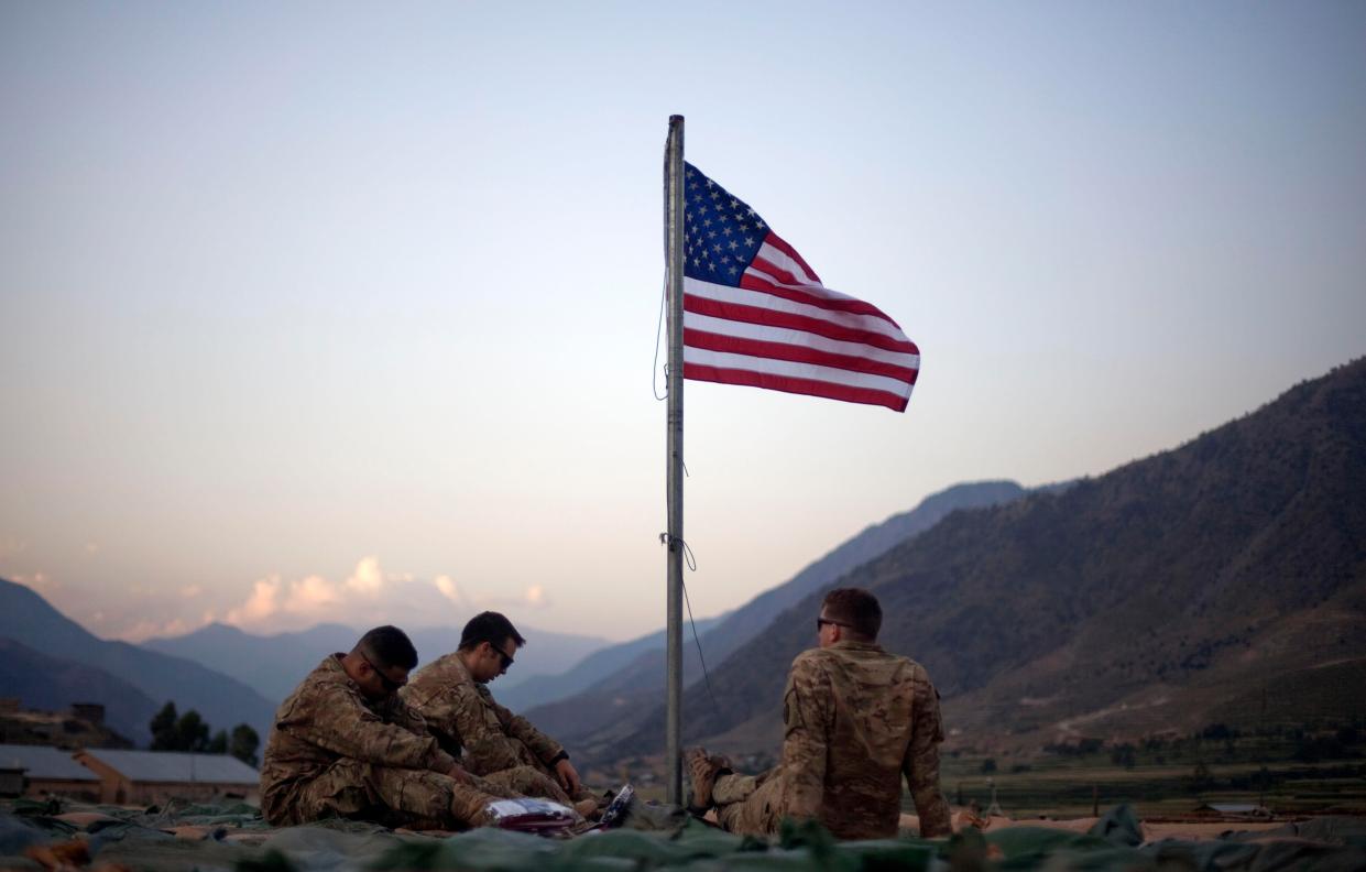 U.S. Army soldiers sit beneath an American flag raised to commemorate the tenth anniversary of the 9/11 attacks on Sept. 11, 2011 at Forward Operating Base Bostick in Kunar province, Afghanistan. (AP Photo/David Goldman)