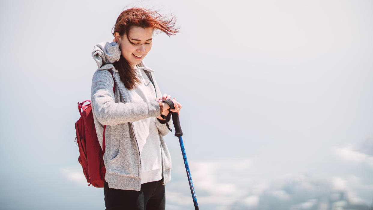  Woman using smartwatch and trekking pole while hiking 