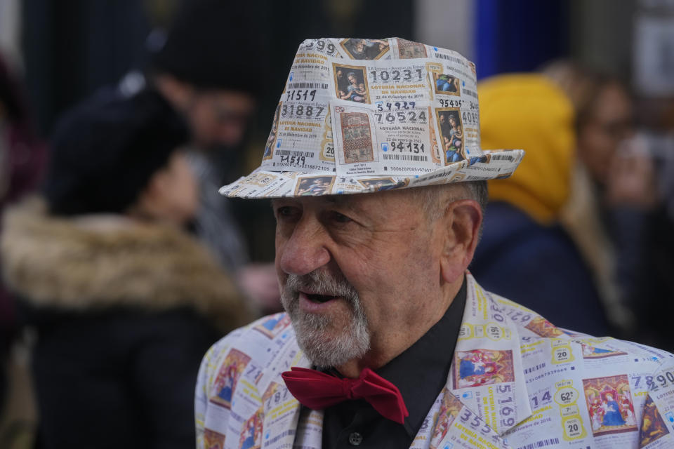 A man with a suit and hat decorated in printed lottery tickets stands outside the famous Doña Manolita lottery ticket shop in downtown Madrid, Spain, Wednesday, Dec. 21, 2022. People are buying last minute Christmas lottery tickets for Spain's bumper Christmas lottery draw known as El Gordo, or The Fat One, which will be held on Dec. 22. (AP Photo/Paul White)