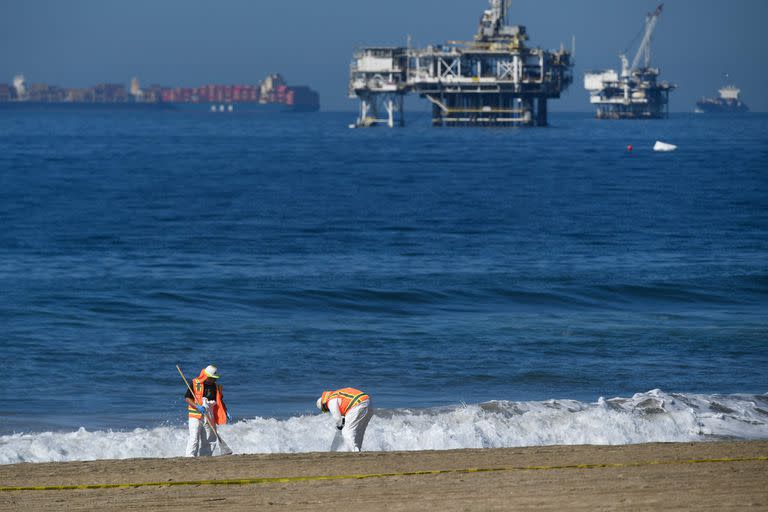 Los buques portacontenedores y las plataformas petroleras se encuentran en el horizonte mientras las tripulaciones ambientales limpian los escombros en la playa después de un derrame de petróleo en el Océano Pacífico en Huntington Beach, California, el 5 de octubre de 2021