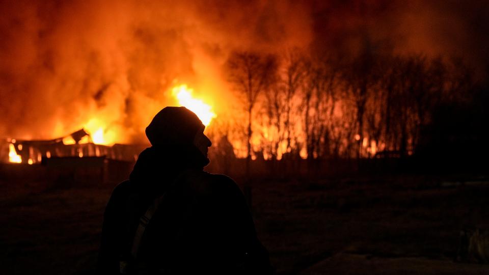 A Ukrainian serviceman is backdropped by a blaze at a warehouse after a bombing on the outskirts of Kyiv, Ukraine, on March 17, 2022.