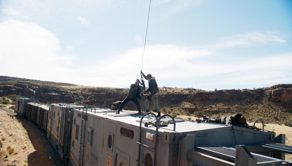 A behind the scenes photo of Dylan O'Brien being put in a harness for a stunt on top of a train