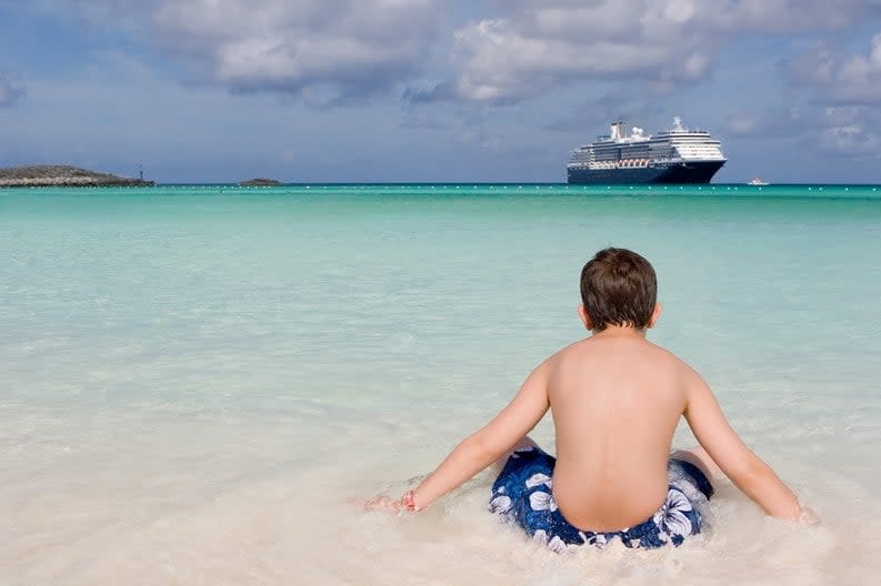 Child on shore of beach with cruise ship off in the distance.