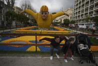 Tourists pose for pictures in front of a sculpture made of lemons during the 90th edition of the Lemon Festival in Menton, France, Friday, March 1, 2024. (AP Photo/Daniel Cole)