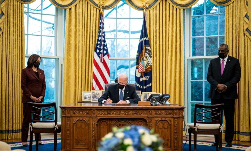 Flanked by Vice President Kamala Harris and Secretary of Defense Lloyd Austin, President Joe Biden signs an executive order in the Oval Office of the White House repealing the ban on transgender people serving openly in the military.