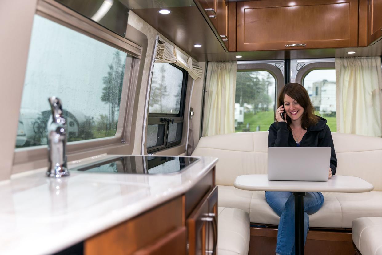 young woman talking on phone and using laptop inside motorhome