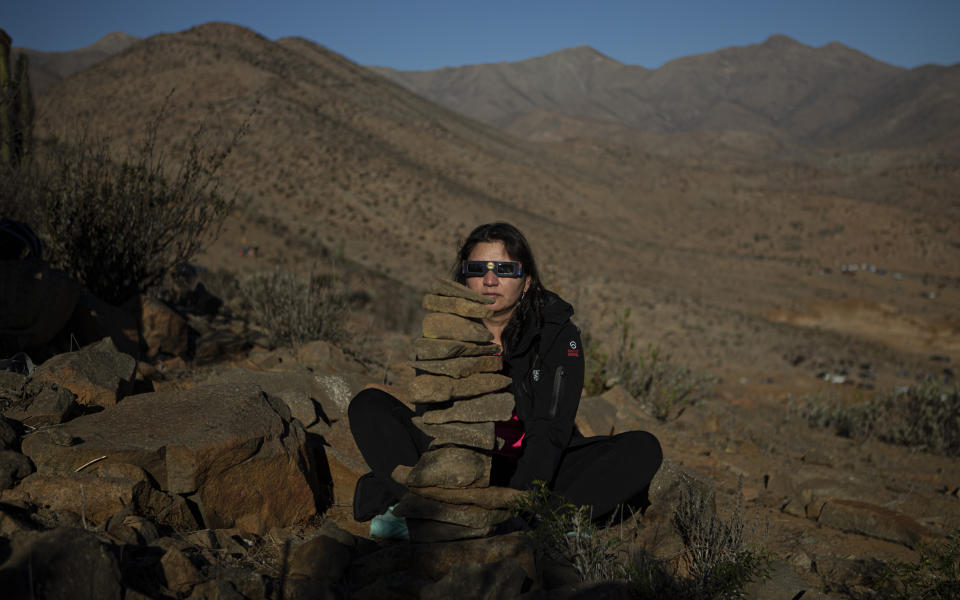 Matilde Pizarro sits behind rocks she arranged into a column during a total solar eclipse in La Higuera, Chile, Tuesday, July 2, 2019. Pizarro said the rock column is known locally as a "Apacheta," and is an indigenous Aymara custom through to bring balance to one's friends and family. (AP Photo/Esteban Felix)