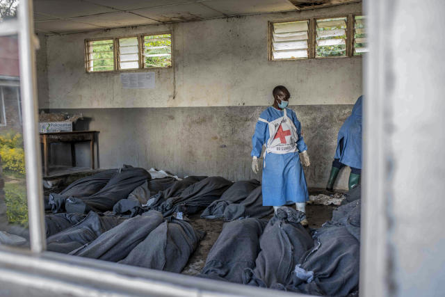 A Red Cross worker stands next to bodies at a makeshift morgue at a primary school in Bushushu, South Kivu province, Congo, Saturday, May 6, 2023. The death toll from flash floods and landslides in eastern Congo has risen to 176, with some 100 people still missing, according to a provisional assessment given by the governor and authorities in the country's South Kivu province. (AP Photo/Moses Sawasawa)