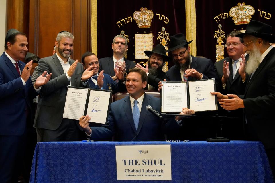Surrounded by state legislators and Jewish leaders, Florida Gov. Ron DeSantis, center, holds up two bills that he signed, Monday, June 14, 2021, at the Shul of Bal Harbour, a Jewish community center in Surfside, Fla. DeSantis visited the South Florida temple to denounce anti-Semitism and stand with Israel, while signing a bill into law that would require public schools in his state to set aside moments of silence for children to meditate or pray.