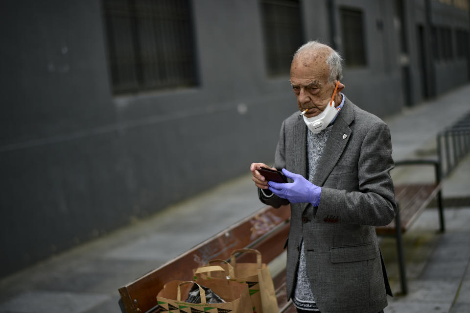 An elderly man partially covers his face with a mask protection to prevent the spread of the coronavirus, as he smokes a cigarette, in Pamplona, northern Spain, Saturday, May 2, 2020. Spain relaxed its lockdown measures Saturday, allowing people of all ages to leave their homes for short walks or exercise for the first time since March 14. (AP Photo/Alvaro Barrientos)