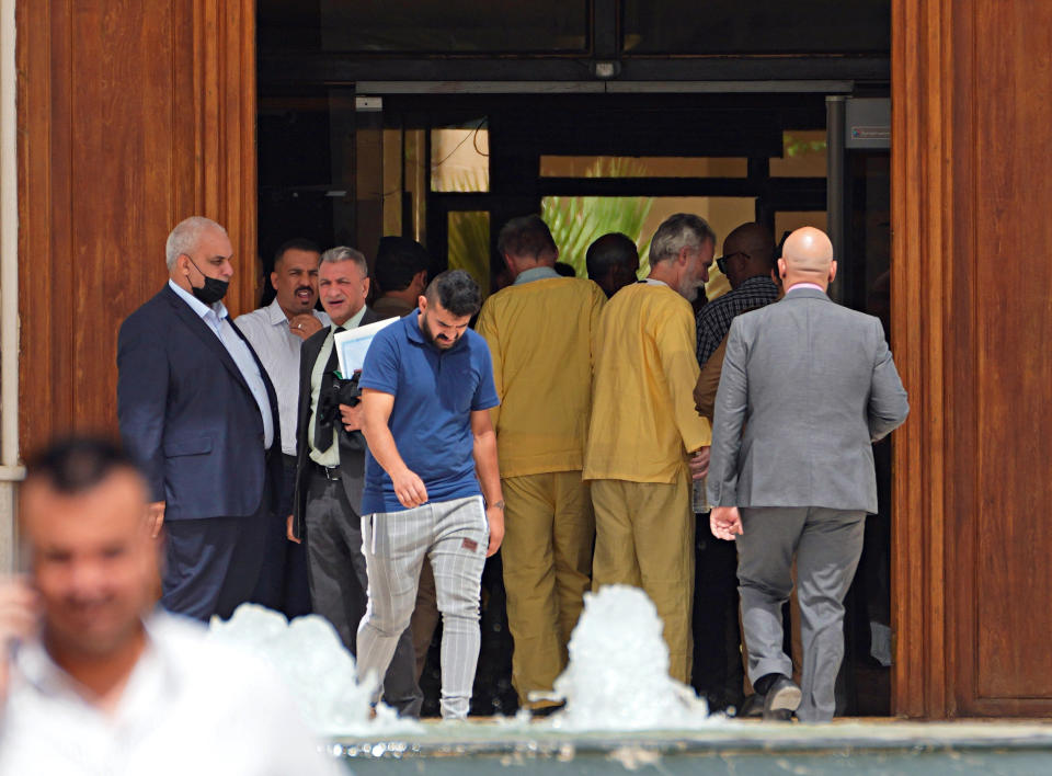 Jim Fitton, center right and Volker Waldman, center left, are handcuffed outside a courtroom in Baghdad, Iraq, Monday, June 6, 2022. The Iraqi court sentenced Fitton, a British citizen, to 15 years in prison on charges of smuggling artifacts out of the country. A German national tried with Fitton was found not to have had criminal intent in the case and will be released. (AP Photo/Hadi Mizban)