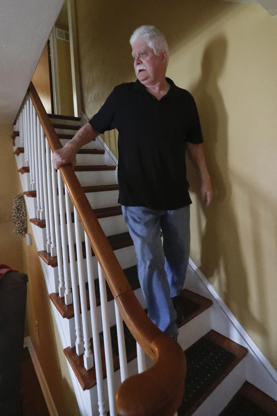 In this April 8, 2019, photo Chuck Pope, who suffers from rheumatoid arthritis, walks down the stairs in his home in Derry, Pa. While he was still working, his insurance covered an injected drug that relieves pain and stops irreversible joint damage but retails for over $5,000 a month. Now his Medicare plan doesn't cover the drug, and Pope says his condition is deteriorating without it. Meanwhile, sales of approved, cheaper versions have been blocked. (AP Photo/Keith Srakocic)