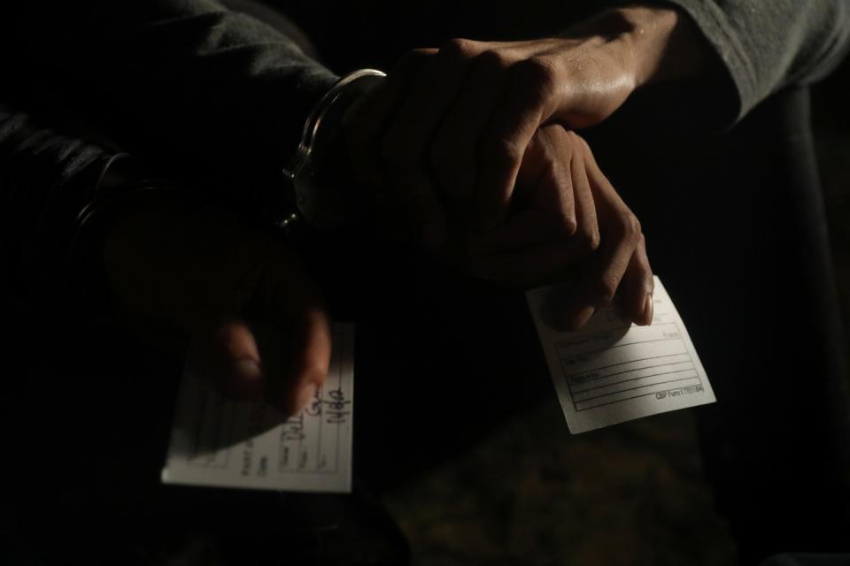 Handcuffed migrants hold processing cards