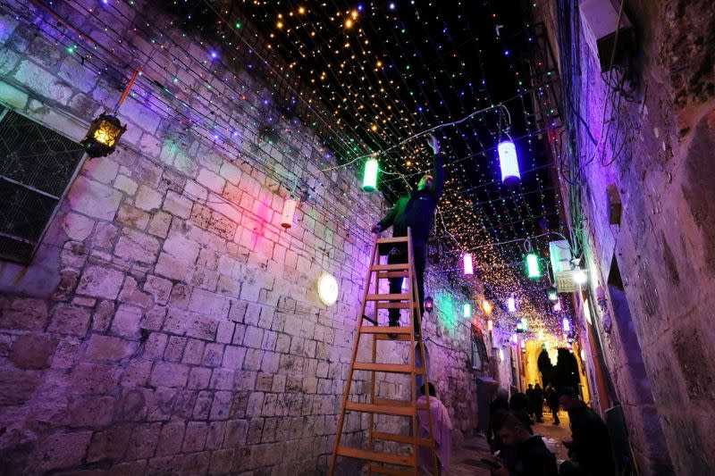 Un hombre coloca luces decorativas en un pasaje en la Ciudad Vieja de Jerusalén como parte de los preparativos para el mes sagrado musulmán del Ramadán, en medio de una flexibilización de las restricciones por la pandemia de coronavirus