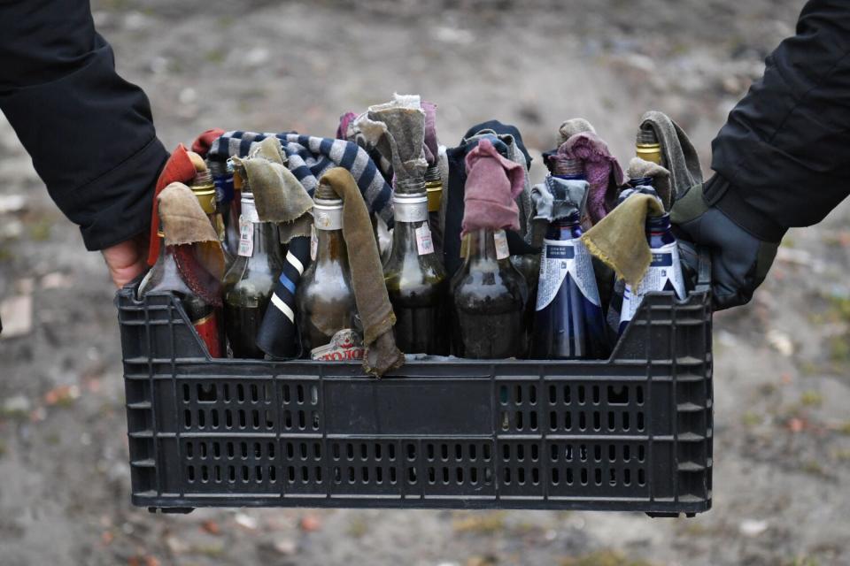 People hold a crate of bottles plugged with rags.