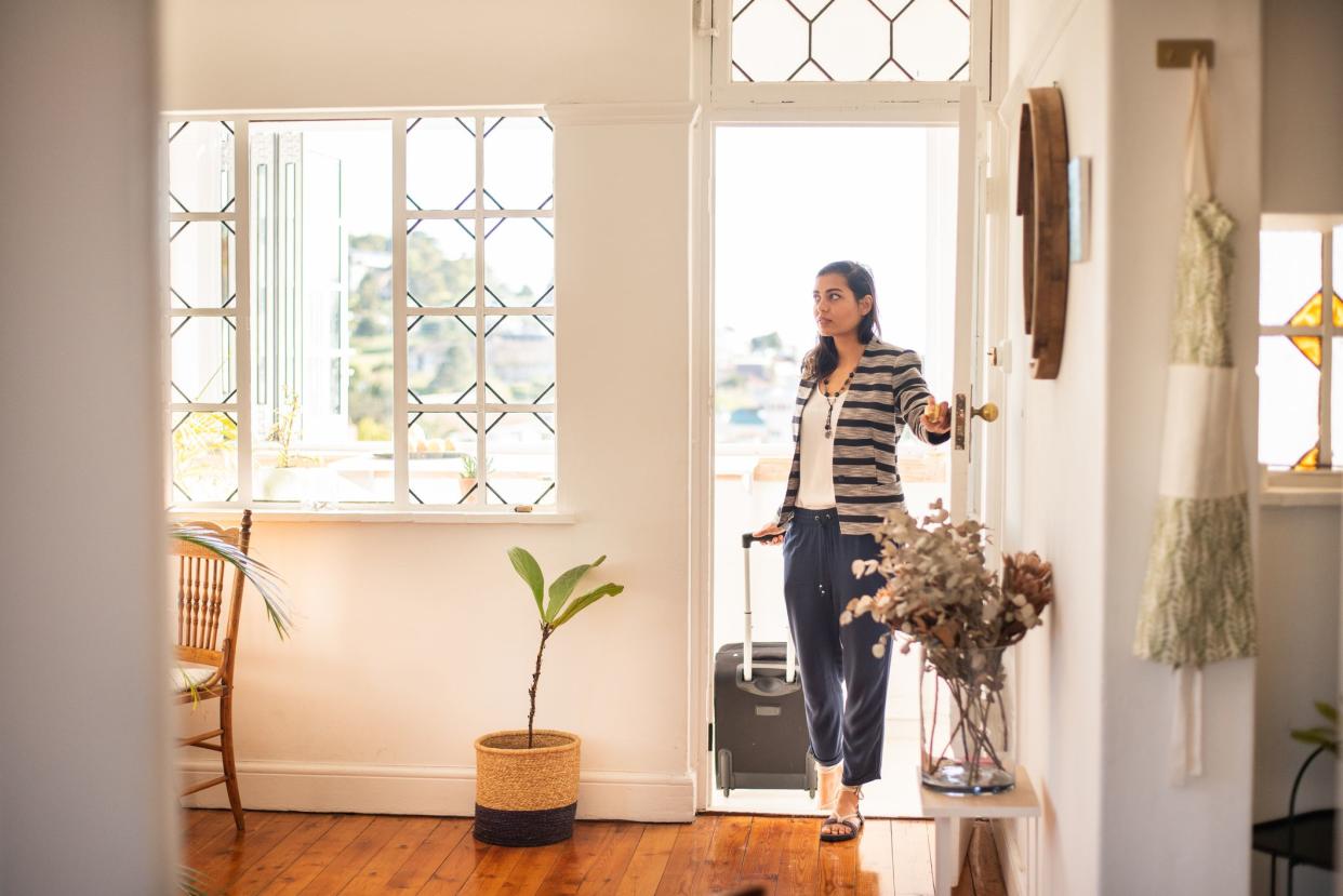 Young woman pulling a suitcase opening the front door of her rental accommodation during a vacation trip