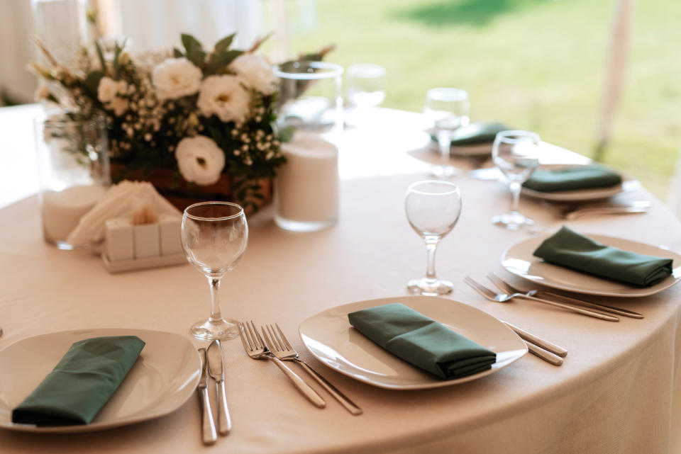 A wedding reception table is elegantly set with plates, silverware, green napkins, wine glasses, and a floral centerpiece