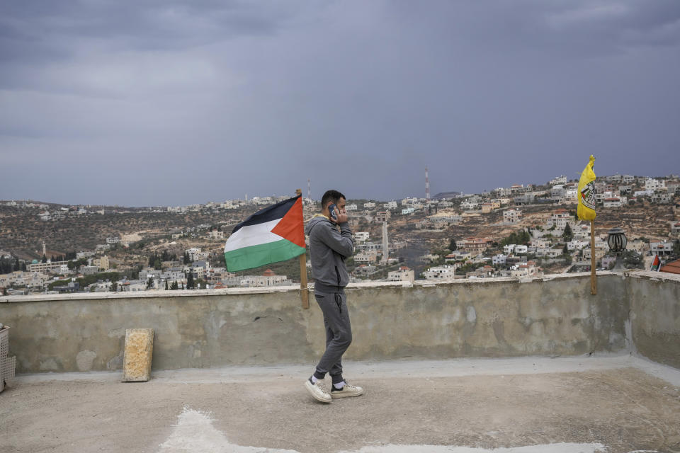 The son of Abdelazim Wadi, whose uncle and cousin were killed by Israeli settlers during a funeral procession on Oct. 12, takes a phone call from the roof of his home beside the Palestinian flag and the flag of the secular nationalist Fatah party in the rural Palestinian village of Qusra, West Bank, Sunday, Nov. 12, 2023. With the world’s attention focused on the fighting in Gaza, Israeli settler violence against Palestinians since Oct. 7 has surged to the highest levels ever recorded by the United Nations. Palestinians say this Israel-Hamas war has left them more scared and vulnerable than ever in recent memory. (AP Photo/Mahmoud Illean)