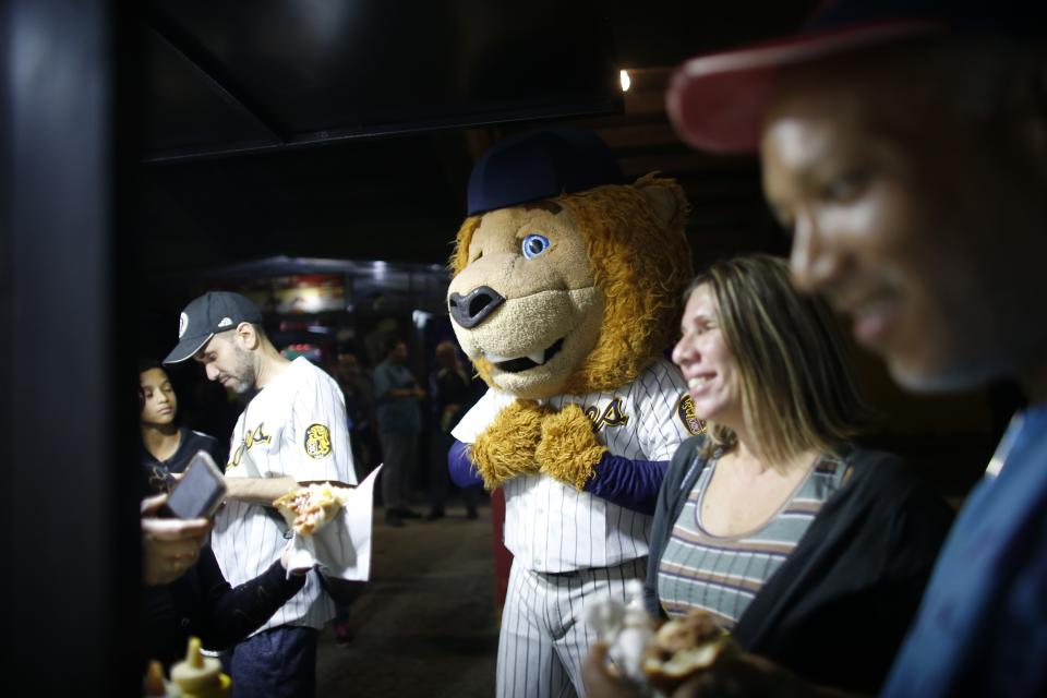 The mascot of Leones de Caracas stands with fans during the opening winter season baseball game between Leones de Caracas and Tigres de Aragua in Caracas, Venezuela, Tuesday, Nov. 5, 2019. In Venezuela, local baseball remains a passion, where for a few hours it’s an oasis for people feeling overwhelmed by life. It’s a safe place to drink beer, hurl insults at players and blow off steam. (AP Photo/Ariana Cubillos)