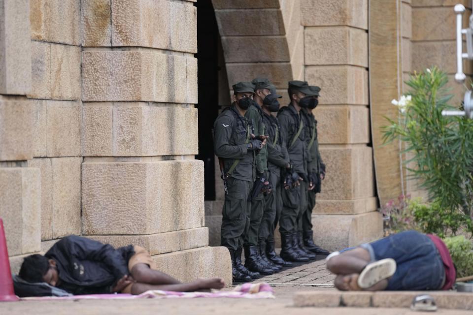 Army soldiers stand guard as protesters sleep by the entrance to president's office in Colombo, Sri Lanka, Friday, July 15, 2022. Protesters retreated from government buildings Thursday in Sri Lanka, restoring a tenuous calm to the economically crippled country, and the embattled president at last emailed the resignation that demonstrators have sought for months. (AP Photo/Eranga Jayawardena)