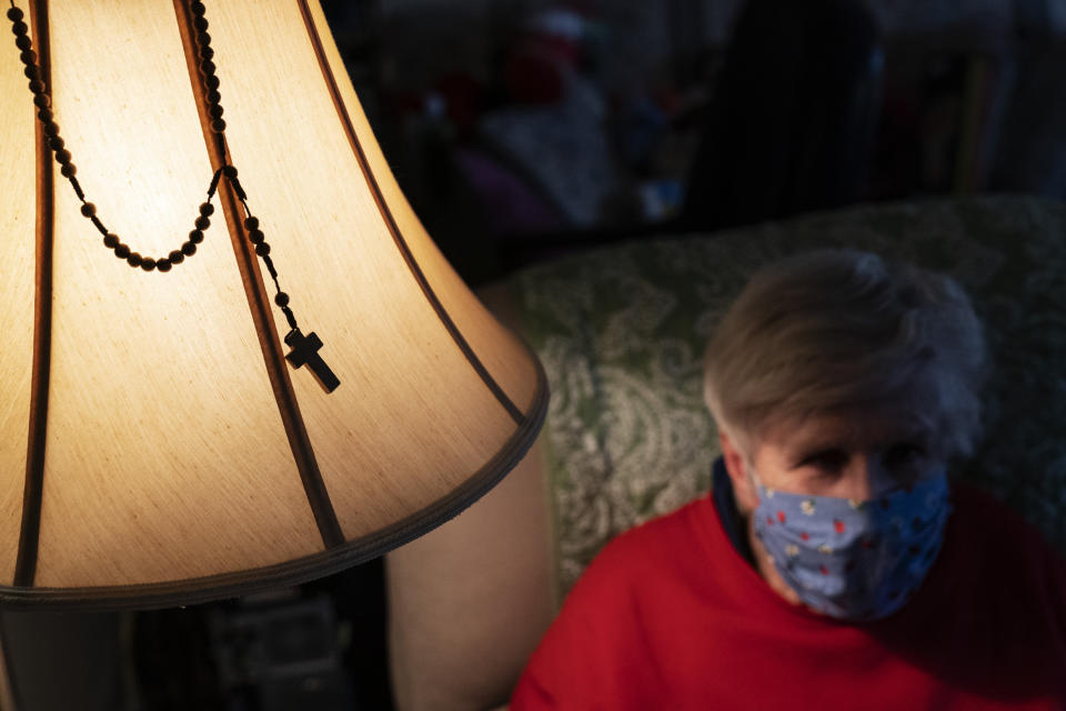 A rosary hangs on a lamp next to Donna Duval, 65, as she sits in her living room during a visit from Meals on Wheels in Pawtucket, R.I, Friday, Nov. 20, 2020. Meals on Wheels of Rhode Island has increased their home delivered meals across the state since the pandemic began from 1,200 to 4,000 meals per day. The organization has had 1,400 inquiries for joining the program since the start of the pandemic, that's well above the normal for a 7-month period. (AP Photo/David Goldman)