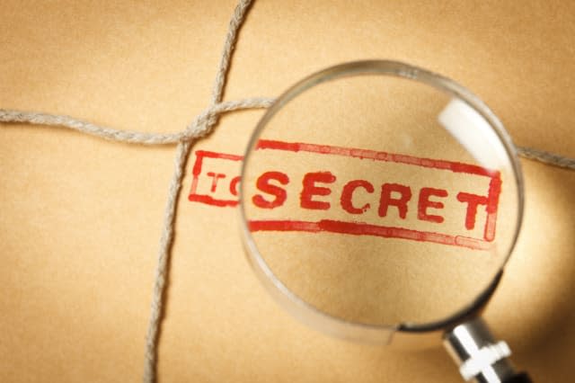 A magnifying glass over a top secret word stamped on a kraft paper envelope closed with a cord. Shallow depth of field due to th