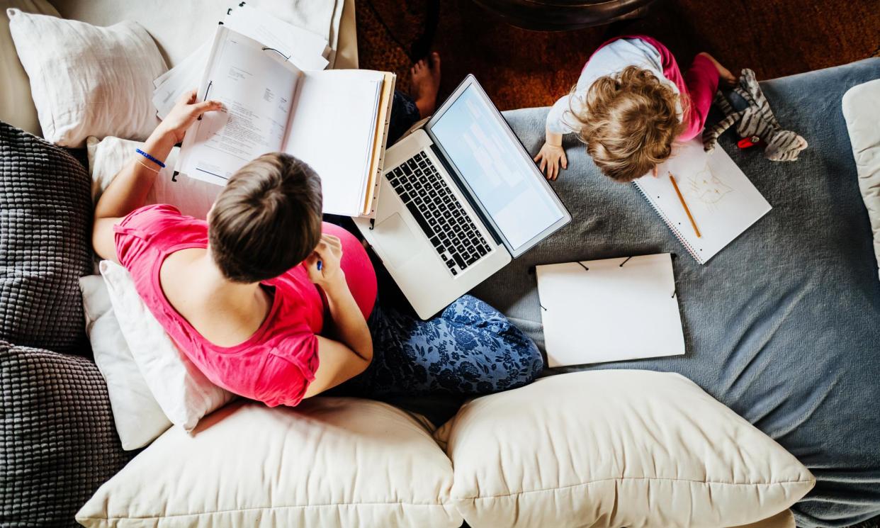 <span>Aerial View Of Mother Working At Home With Toddler<br>An aerial view of a mother working from home on her laptop with her toddler next to her drawing on a paper pad.</span><span>Photograph: Tom Werner/Getty Images</span>