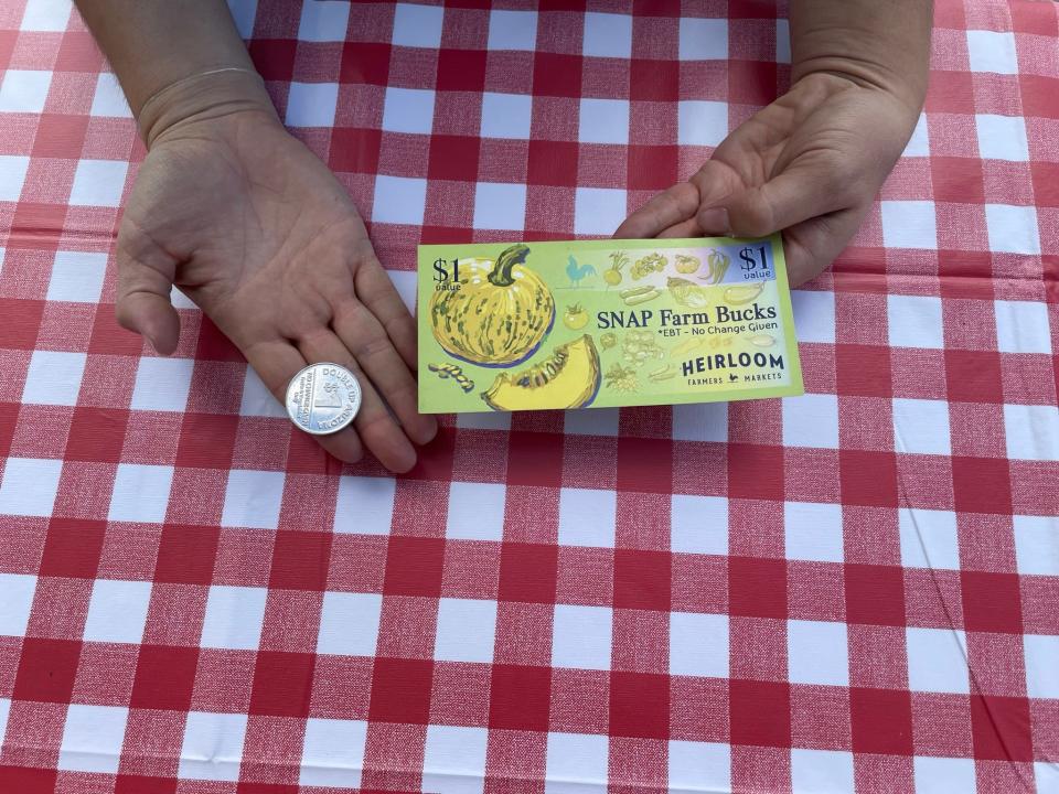 A staff member of Heirloom Farmers Markets holds a "farm buck" and a coin from the Double Up Food Bucks Arizona, a program that incentivizes fruit and vegetable consumption by doubling the amount SNAP participants can spend on local produce.