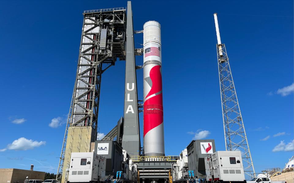 rocket alongside a tower at a launch pad with blue sky in behind