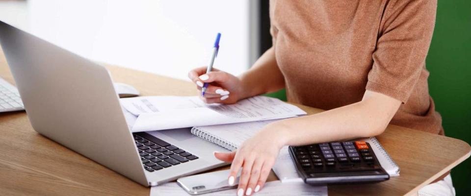 Woman sitting at laptop computer, making notes, calculating expenses.