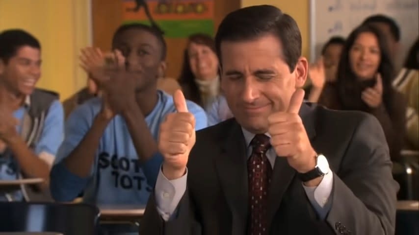 Michael smiling awkwardly with his thumbs up in a classroom with other clapping students in "The Office"