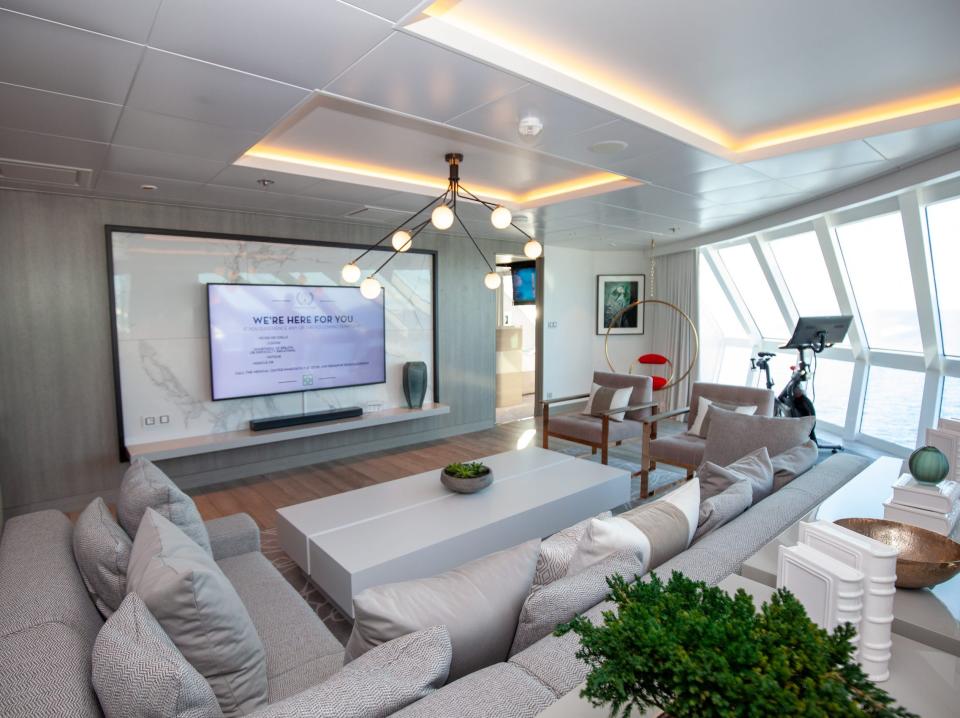 the living room with a large couch facing a TV and a peloton surrounded by windows Iconic suite on the Celebrity Apex cruise ship