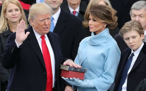 Melania holds the Bible as her husband takes the presidential oath of office in January  - Credit: EPA