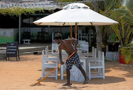 A staff member cleans the sea sand as empty dining tables at Pearl Divers, a diving school, at Unawatuna beach in Galle