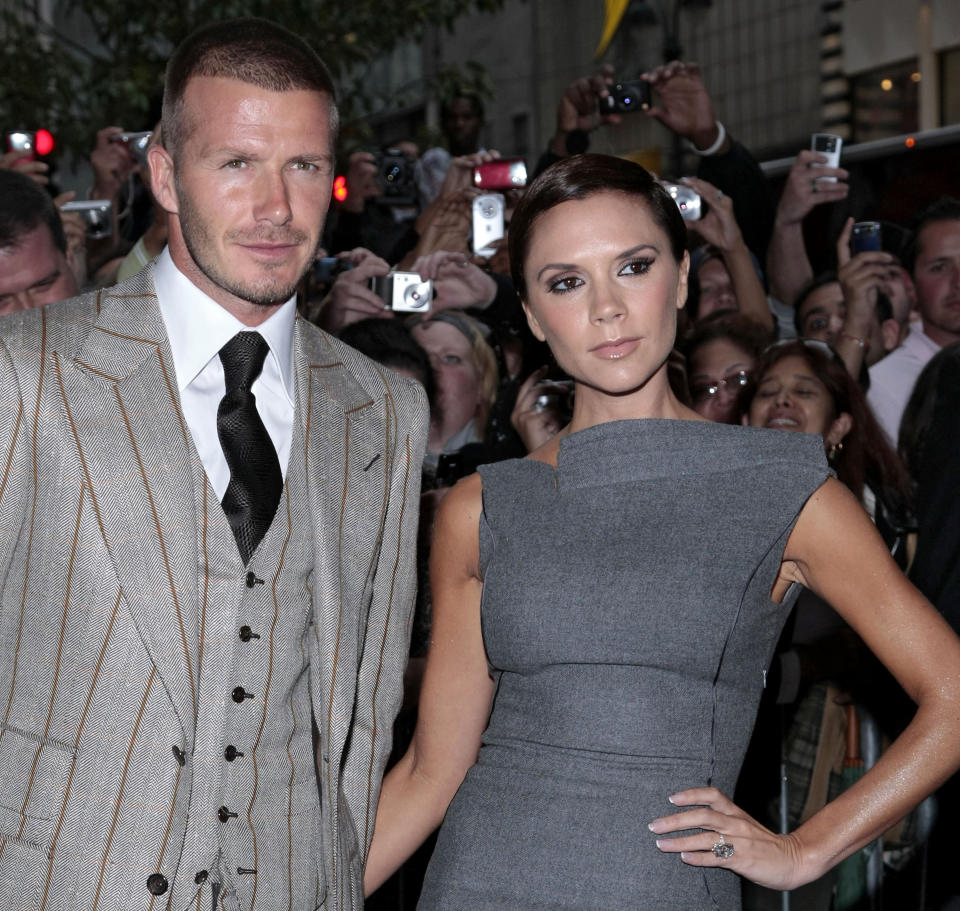 David Beckham, wearing a striped three-piece grey suit, and Victoria Beckham, wearing a grey dress with an asymmetrical neckline, pose for photographs at the launch of their Beckham Signature fragrance