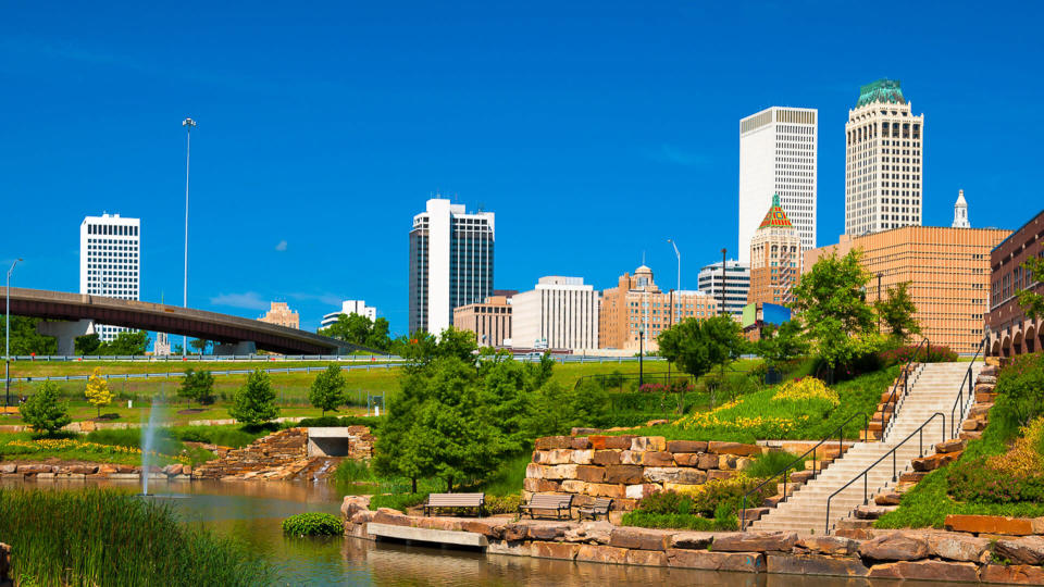 Downtown Tulsa skyline in the background with a park with a waterway and fountain in the foreground.