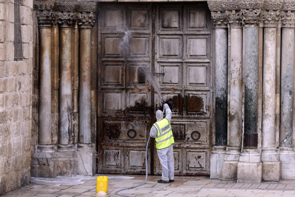 A worker disinfects the doors of the closed Church if the Holy Sepulchre in Jerusalem's Old City, as general public movements are limited to prevent the spread of coronavirus, Monday, March 30, 2020. (AP Photo/Mahmoud Illean)